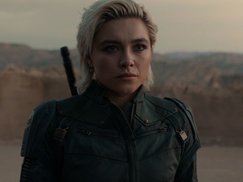 A young woman with short, styled hair wears a dark leather jacket, standing in a barren landscape wi...
