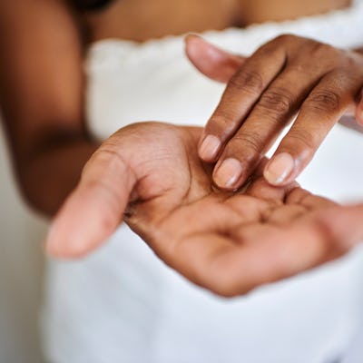 A close-up view of two hands. One hand rests palm-up while the other lightly touches the palm, set against a soft, neutral background.