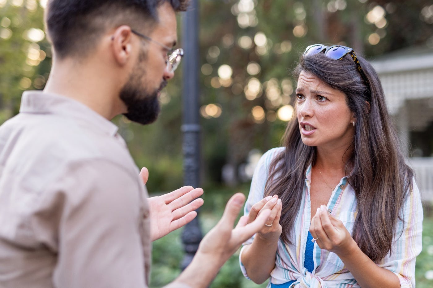 A man and a woman are engaged in a serious conversation outdoors. The woman appears frustrated while expressing her feelings, and the man listens attentively.