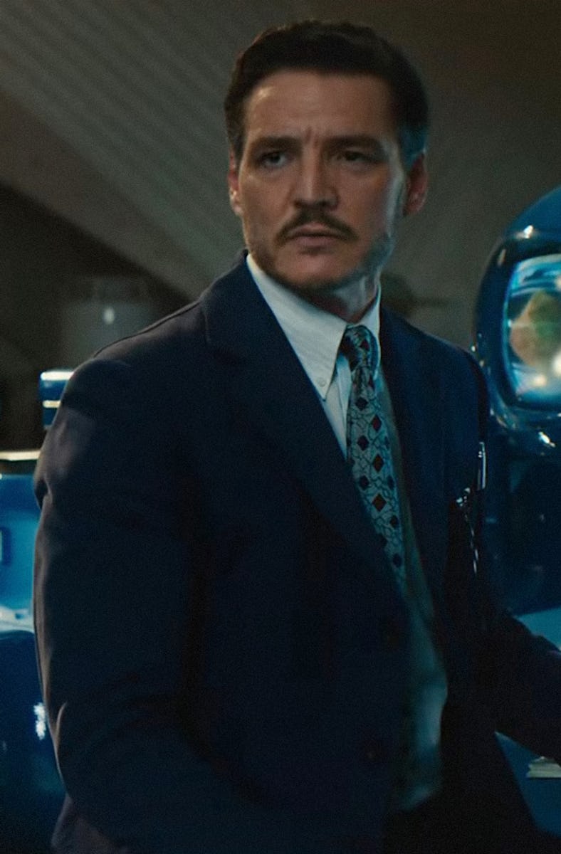 A well-dressed man with a mustache sits near a large, futuristic blue machine in a sleek, modern int...