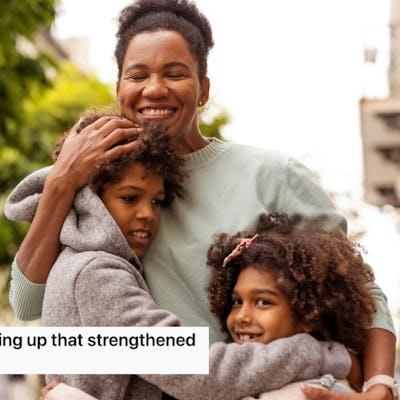 A joyful mother embraces her two children outdoors, with trees and buildings in the background.