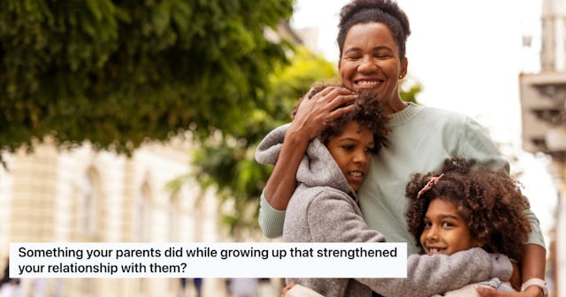 A joyful mother embraces her two children outdoors, with trees and buildings in the background.