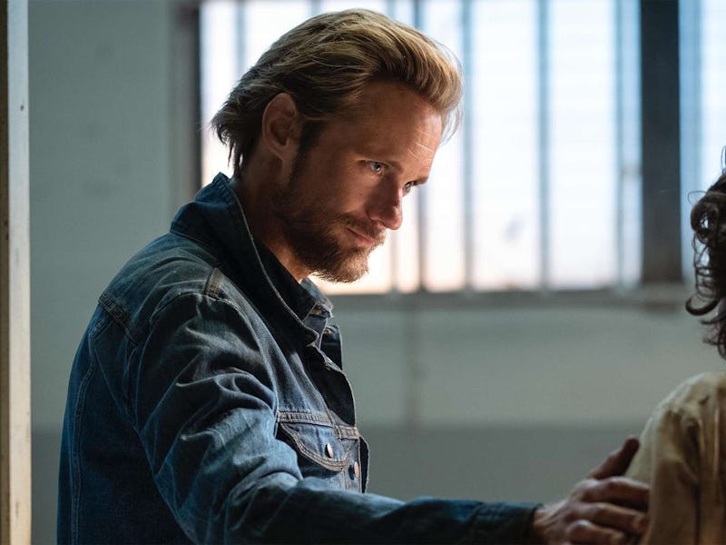 A man with light blonde hair and a beard wears a denim jacket, engaged in a serious conversation, wi...