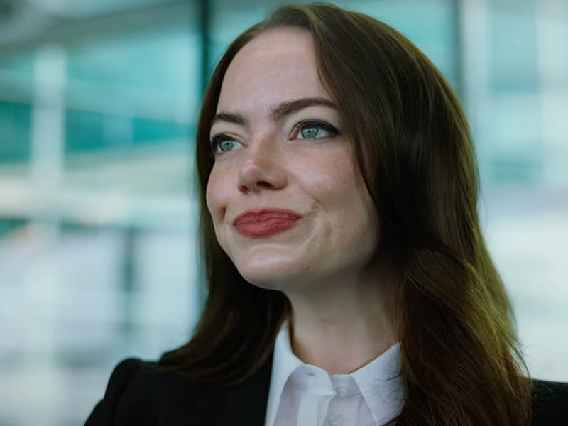 A smiling woman with long brown hair and blue eyes is dressed in a black blazer and white shirt, set...