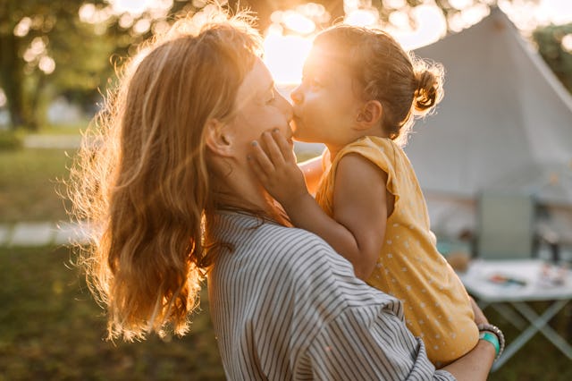 A joyful moment between a mother and child, as the child kisses the mother’s cheek. The warm sunligh...