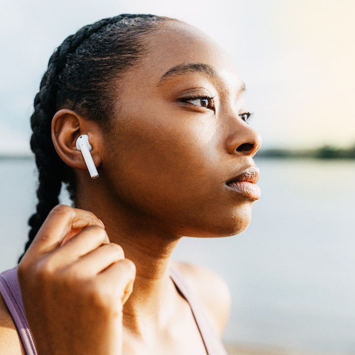 A profile of a young woman with braided hair, wearing wireless earphones, gazing thoughtfully toward...