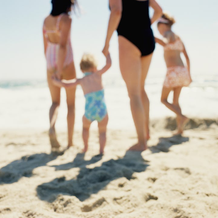 A group of four individuals, including children, walking hand in hand along a sandy beach. The ocean...