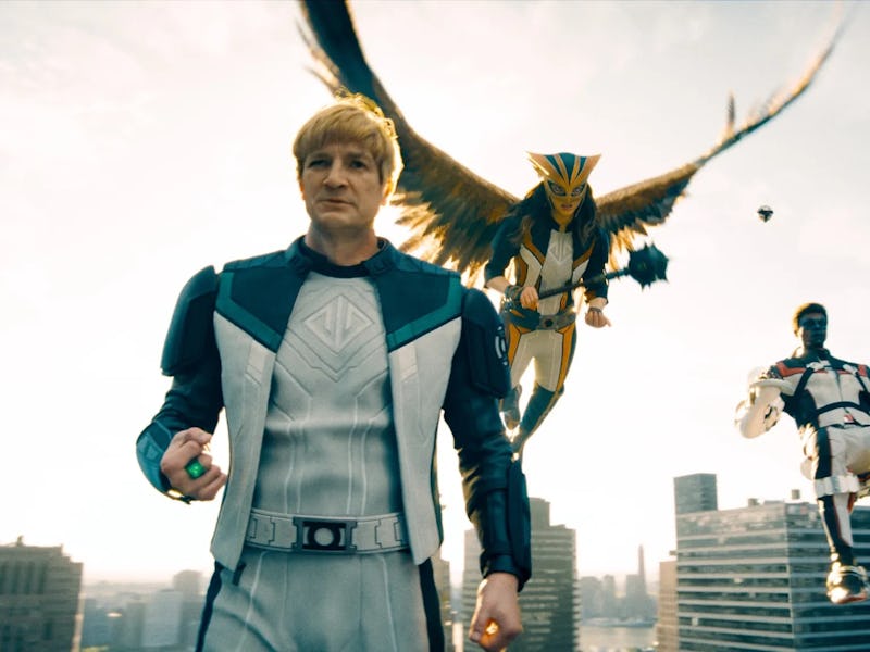 Three superheroes pose on a city rooftop: a man in a gray suit, a winged figure soaring above, and a...