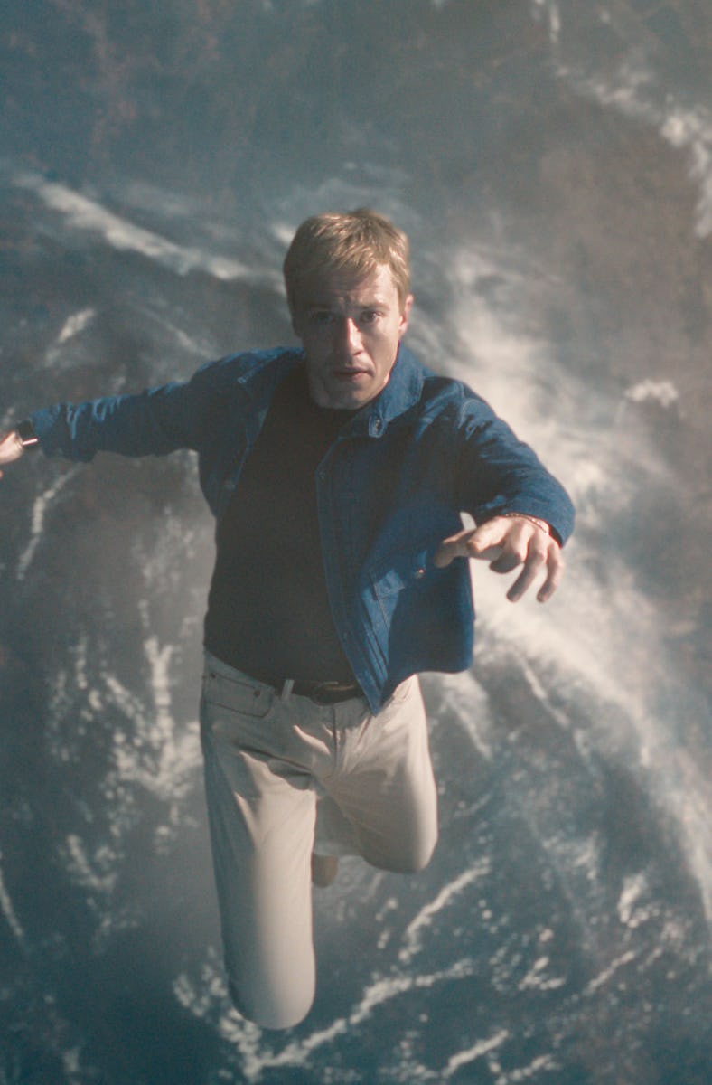 A person in a blue shirt and cream pants is suspended mid-air above Earth, surrounded by clouds, cre...