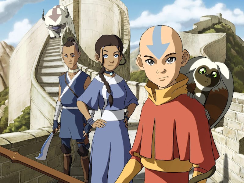 Aang, Katara, and Sokka stand on a stone structure, overlooking a scenic landscape. Aang, in orange ...