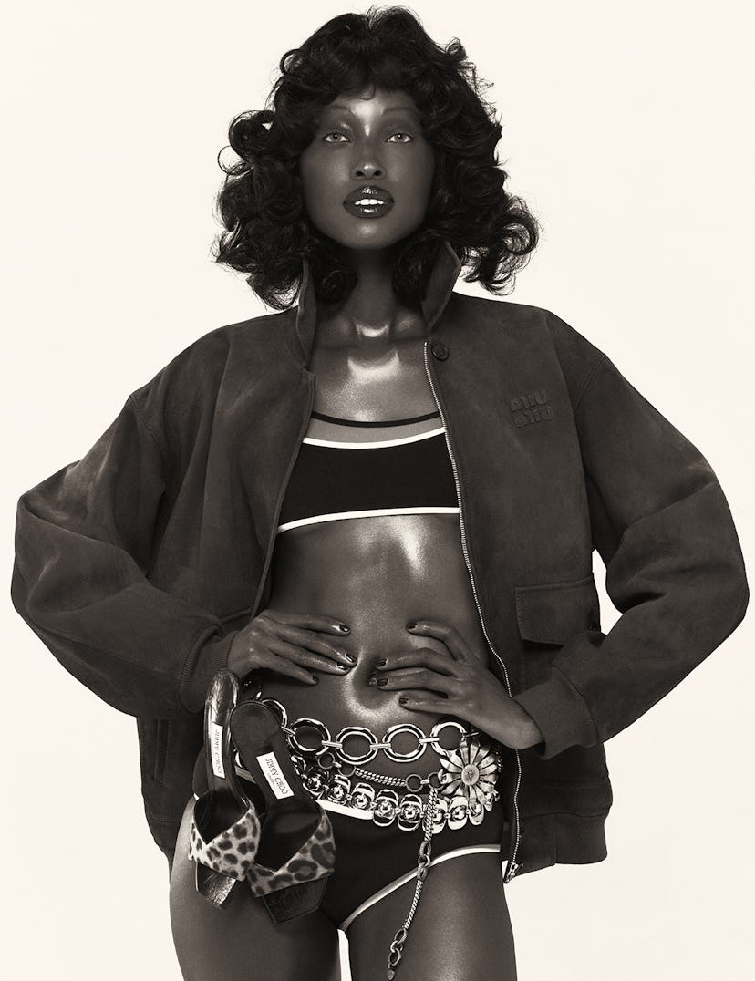 a model with curly shoulder-length hair wearing a bikini with a track jacket. the photo is black and...