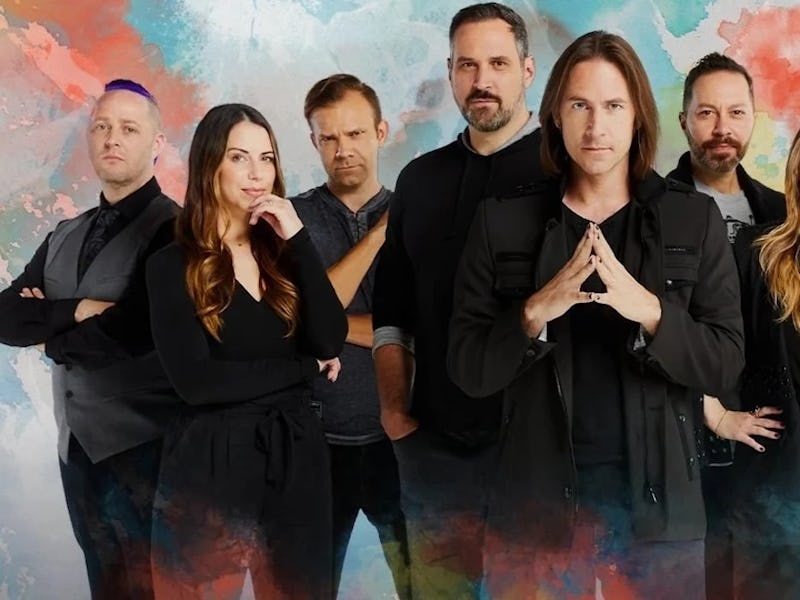 A diverse group of nine individuals stands together in a colorful, artistic background. They are sty...