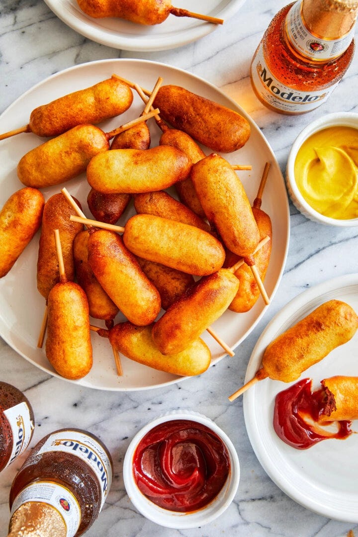 Homemade mini corn dogs surrounded by condiments and beers, one of the best winter olympics party fo...