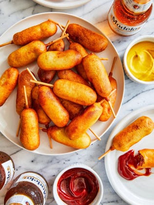 Homemade mini corn dogs surrounded by condiments and beers, one of the best winter olympics party fo...