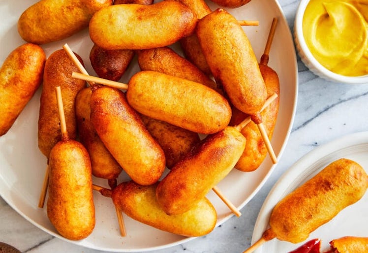 Homemade mini corn dogs surrounded by condiments and beers, one of the best winter olympics party fo...