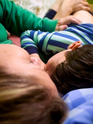 A person and a child lie close together on a bed, both facing the same direction. The child is weari...