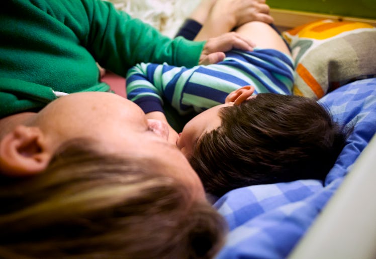 A person and a child lie close together on a bed, both facing the same direction. The child is weari...