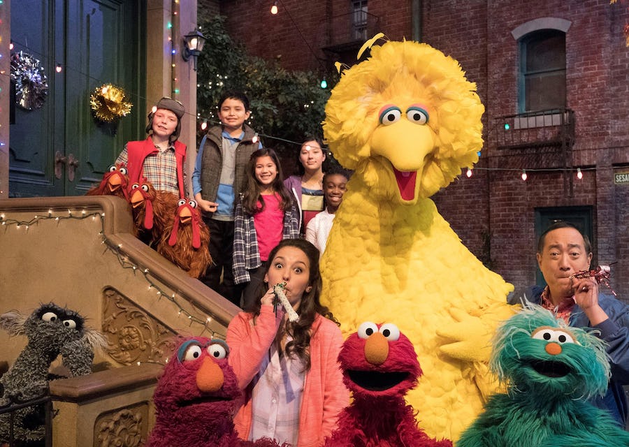 Big Bird and friends stand on a stoop on Sesame Street. 
