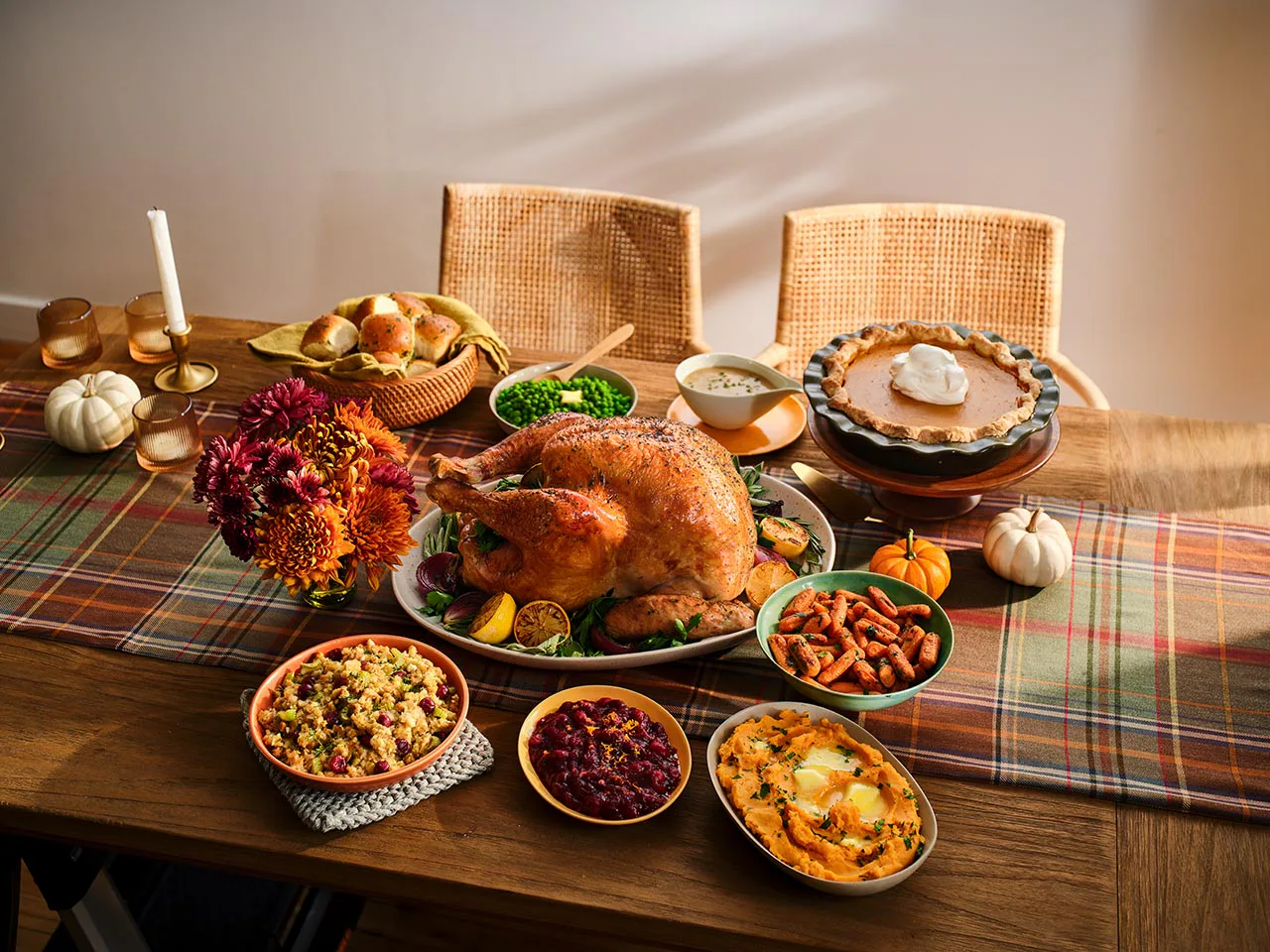 Thanksgiving meal with turkey, pumpkin pie, rolls, and more sides spread on the table.