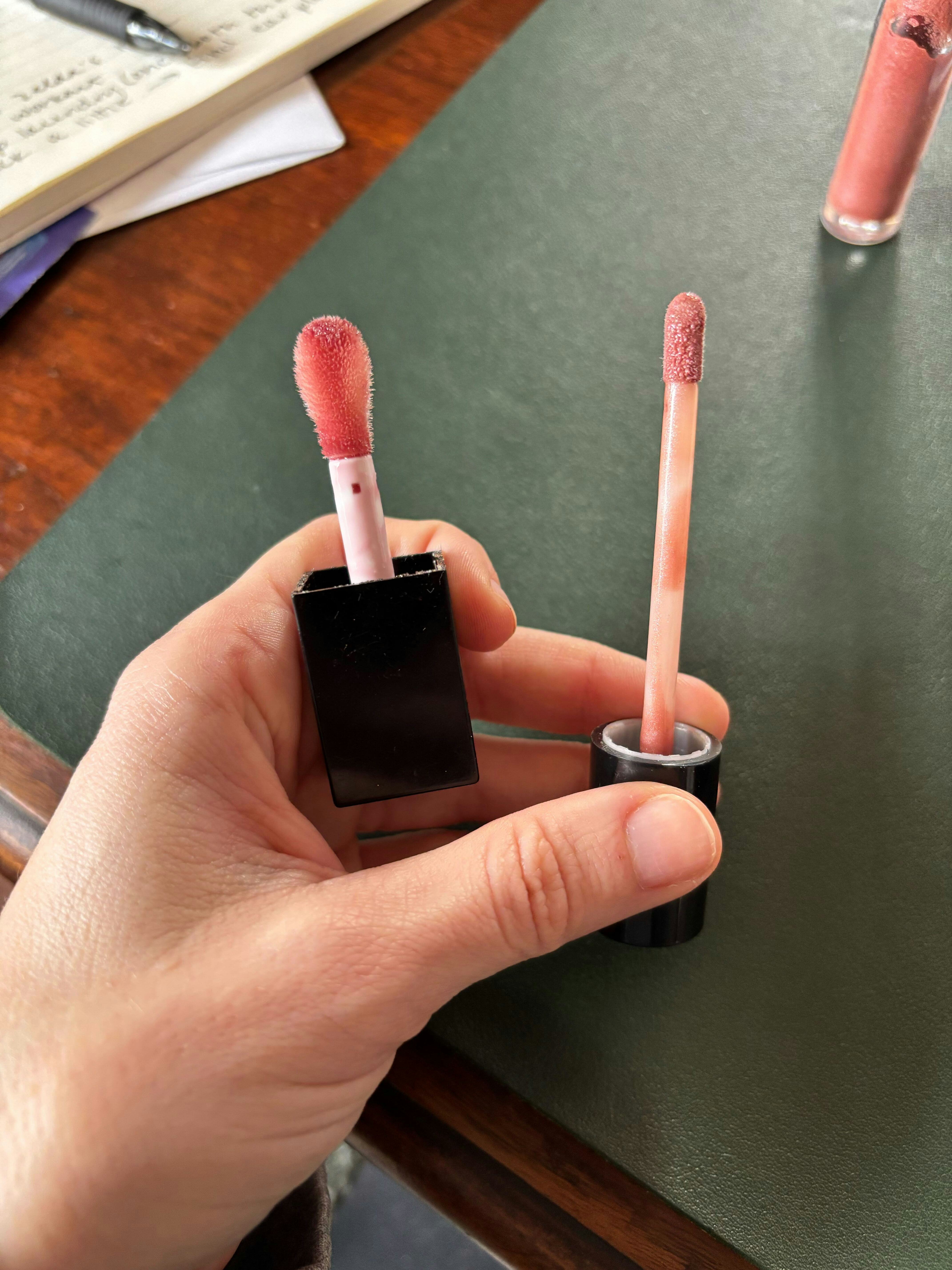 Author holding up two lip gloss applicators for comparison, the one on the left is larger than the s...