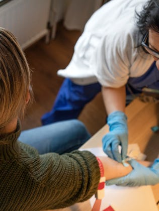 A healthcare worker in blue gloves is extracting blood from a person’s arm using a needle and syring...