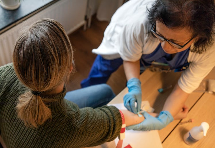 A healthcare worker in blue gloves is extracting blood from a person’s arm using a needle and syring...