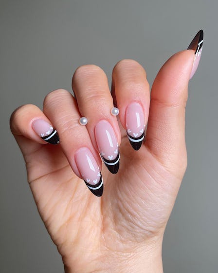 A french manicure with black tips with white stripes and white hearts