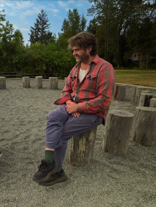 Zach Galifianakis sits on a tree stump talking to a child in a screen still from This Is A Gardening...