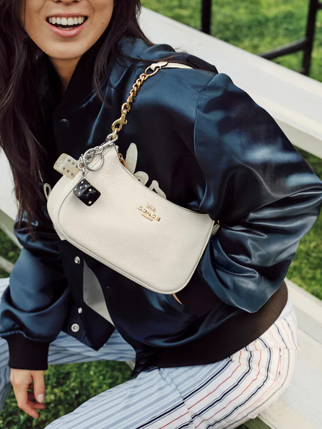 A woman wearing a sporty jacket with the Teri bag in white over her shoulder.