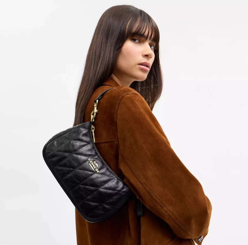 A woman wearing a suede jacket with a quilted black Teri bag over her shoulder.