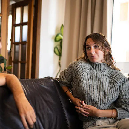 A man and woman are sitting on a couch in a living room. The man is speaking while the woman listens...