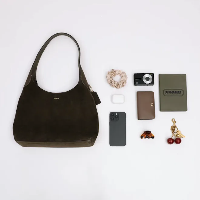 A Coach Brooklyn 34 shoulder bag depicting what can be carried easily inside, including a scrunchie,...