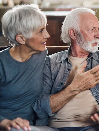 Three adults on a couch: an older white couple arguing with a younger woman holding a smartphone, an...
