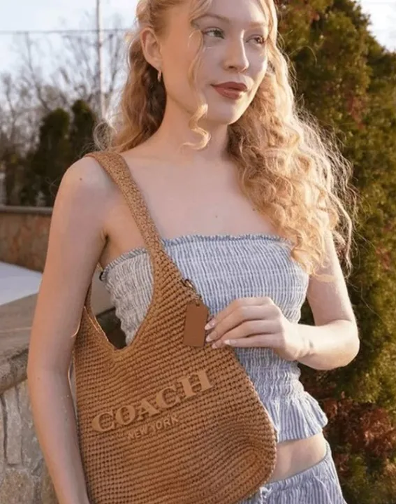 Woman with wavy blond hair holding Coach Brooklyn bag.