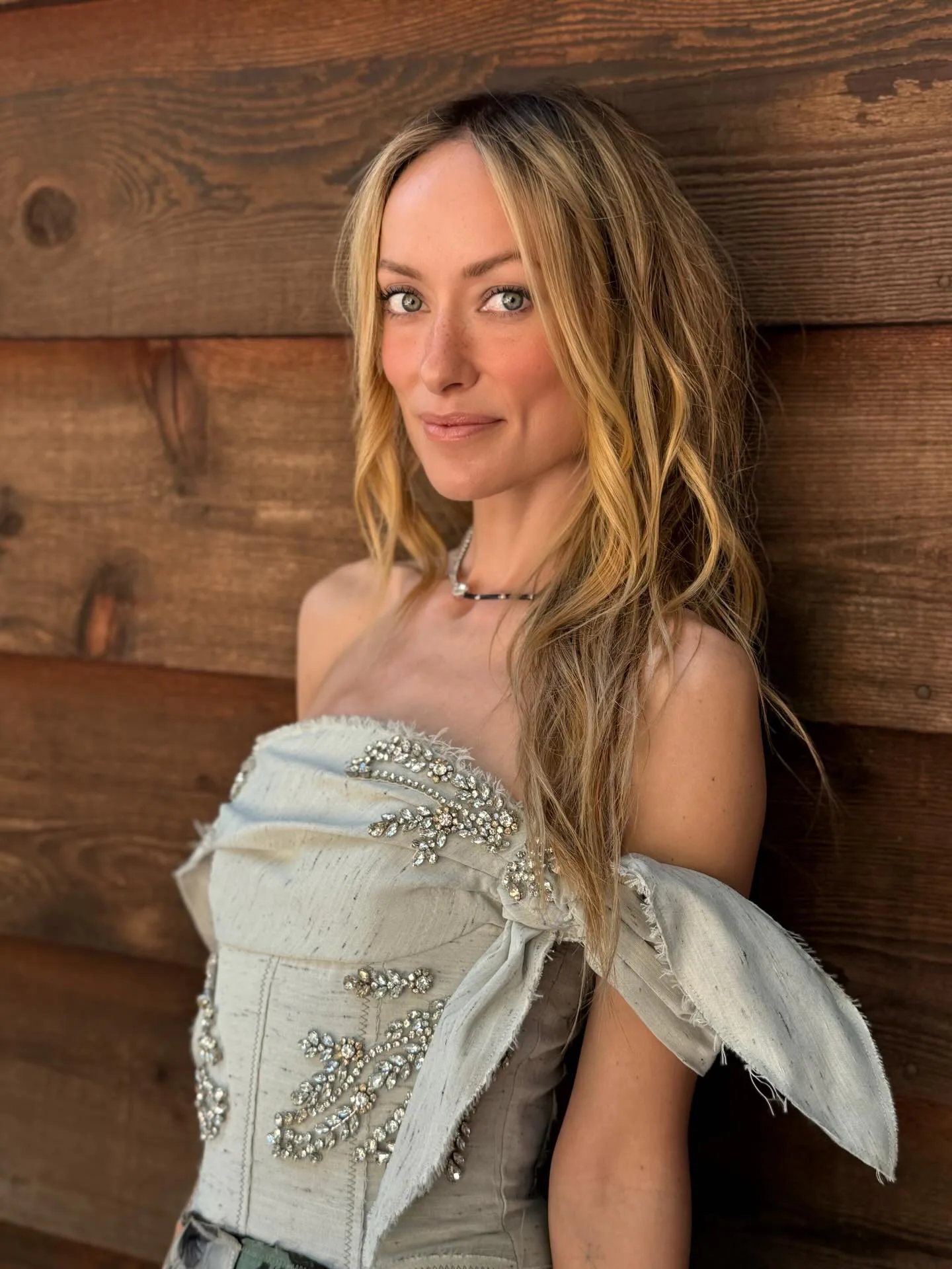 Olivia Wilde wearing a corset standing against a wood wall, her hair long and loose