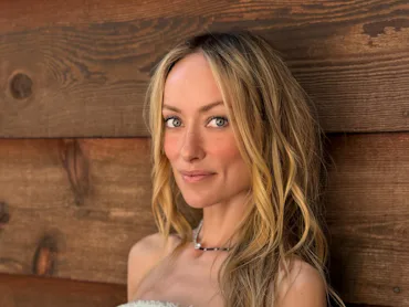 Olivia Wilde wearing a corset standing against a wood wall, her hair long and loose