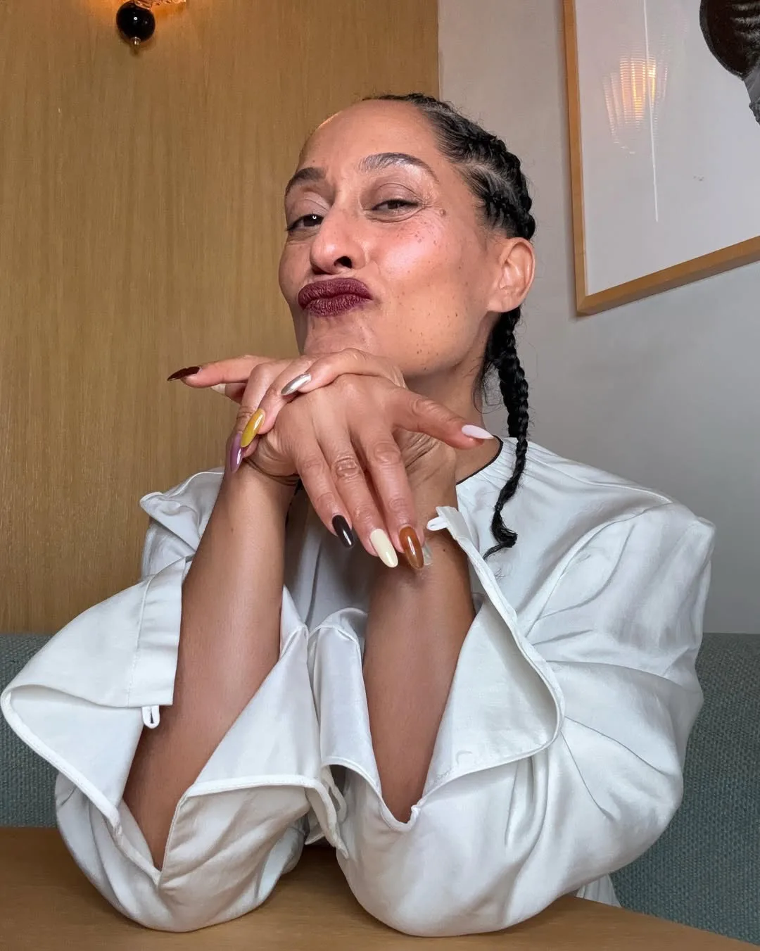 Tracee Ellis Ross with a mismatched manicure, sitting at a table