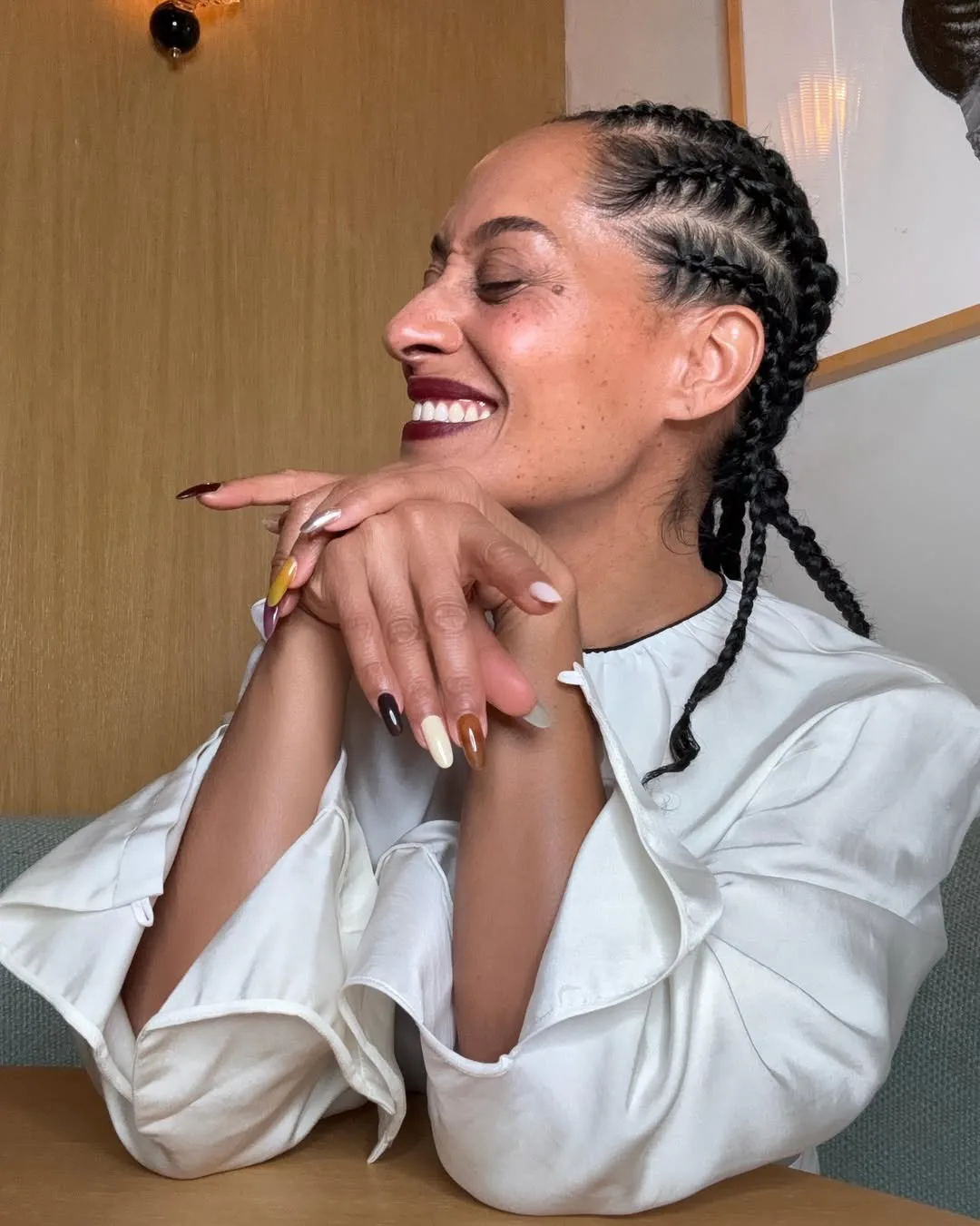 Tracee Ellis Ross with a mismatched manicure, sitting at a table