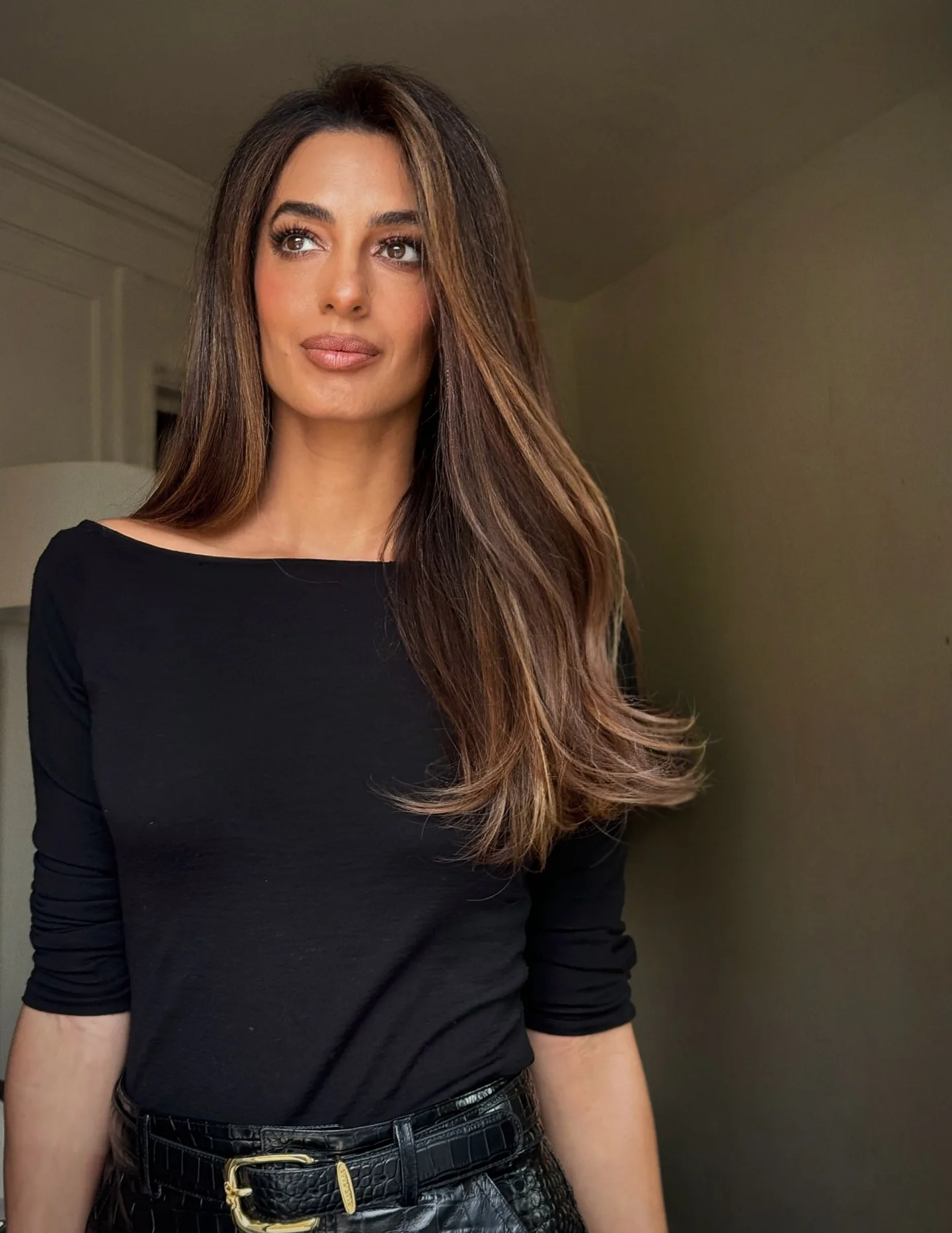 Amal Clooney in a black top, looking away from the camera with long, highlighted hair