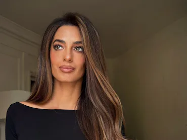 Amal Clooney in a black top, looking away from the camera with long, highlighted hair