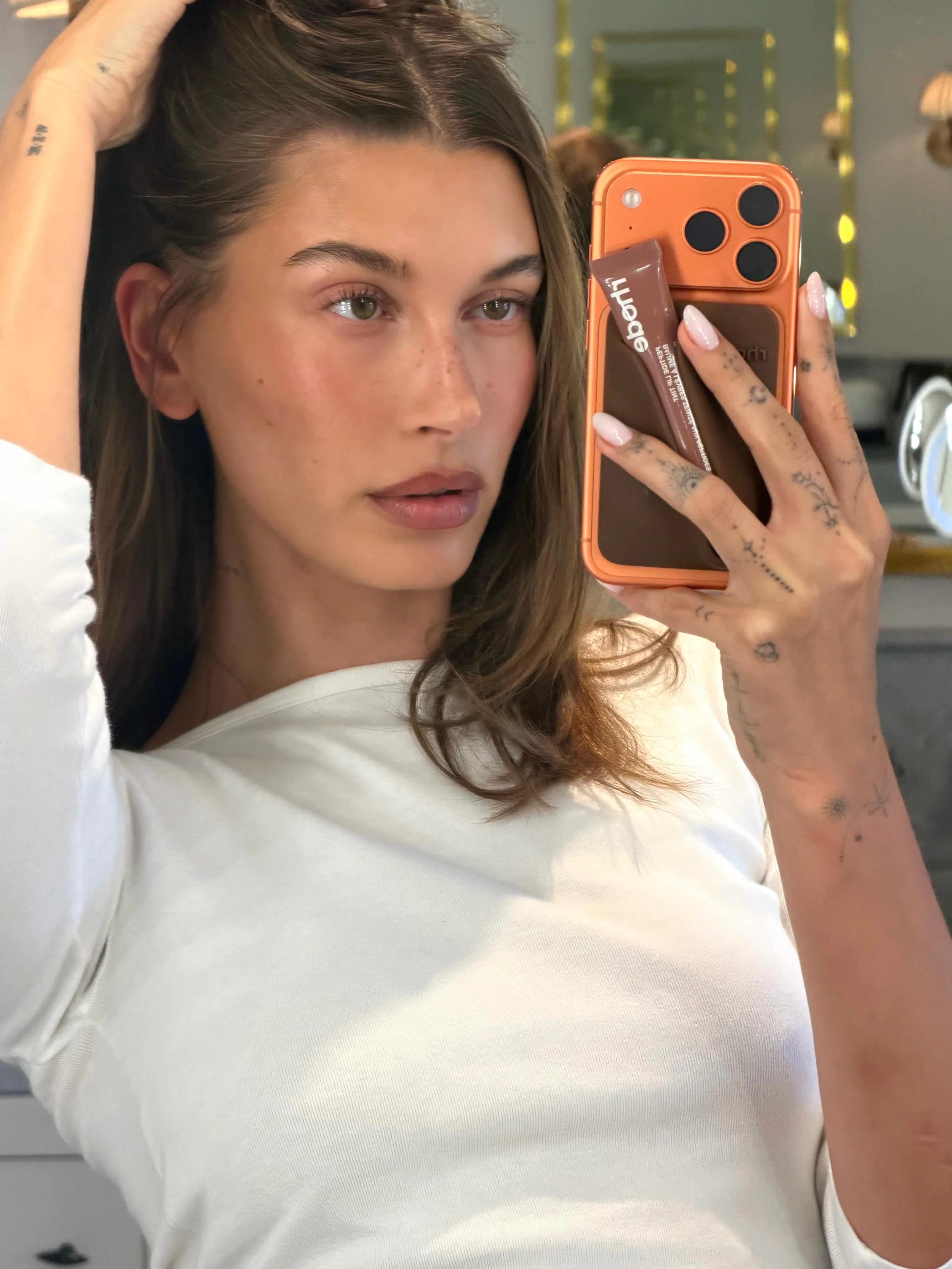 Hailey Bieber taking a mirror selfie, her hand in her hair