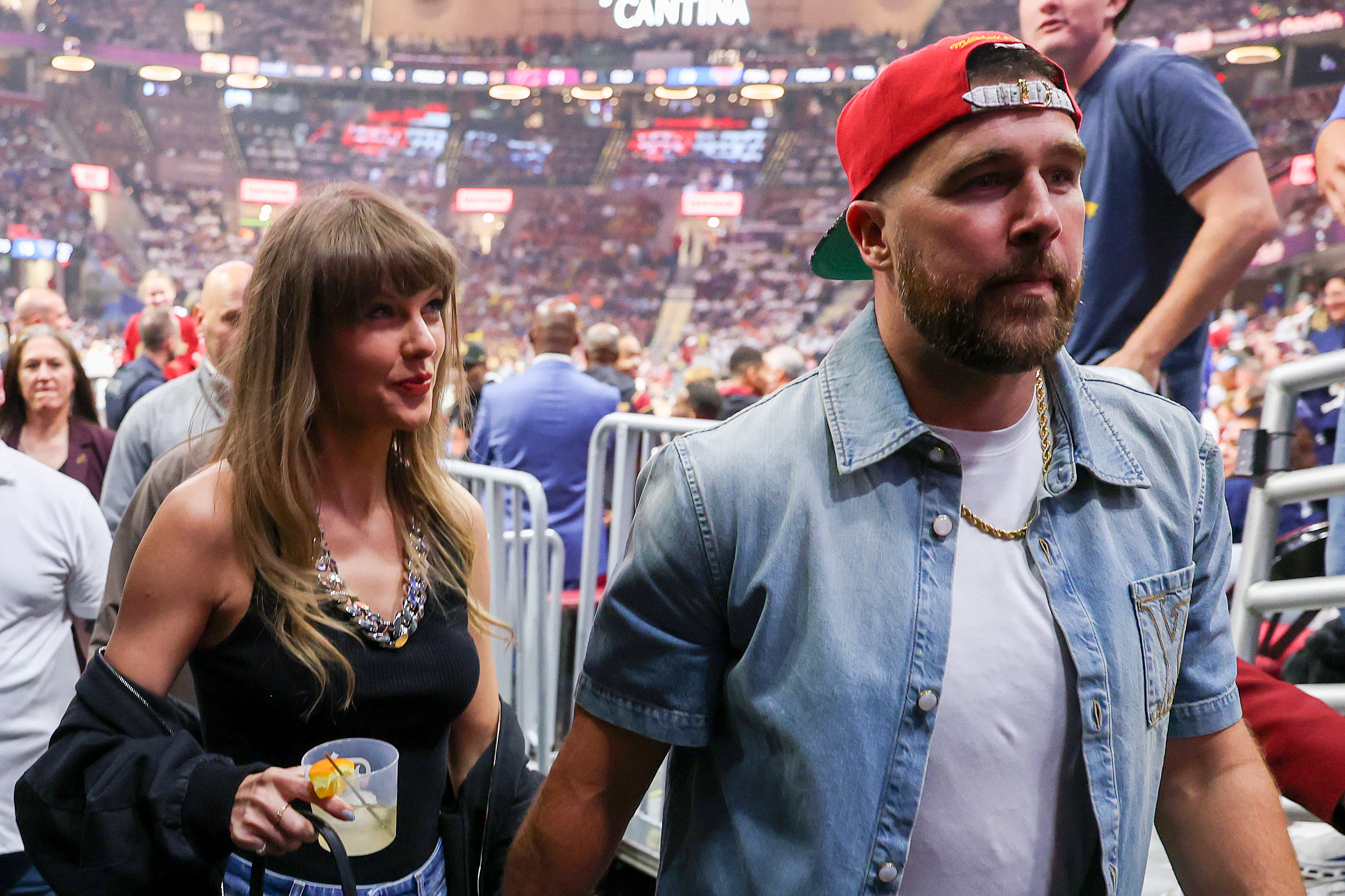 Taylor Swift holding Travis Kelce's hand and a cocktail.