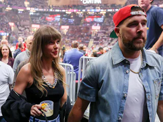 Taylor Swift holding Travis Kelce's hand and a cocktail.