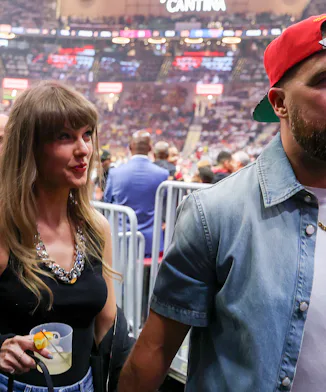 Taylor Swift holding Travis Kelce's hand and a cocktail.