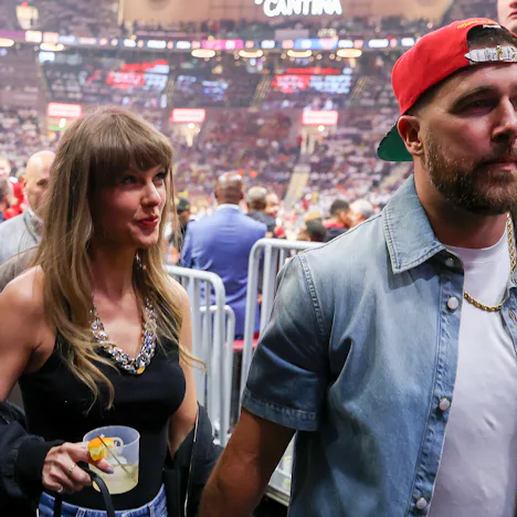 Taylor Swift holding Travis Kelce's hand and a cocktail.