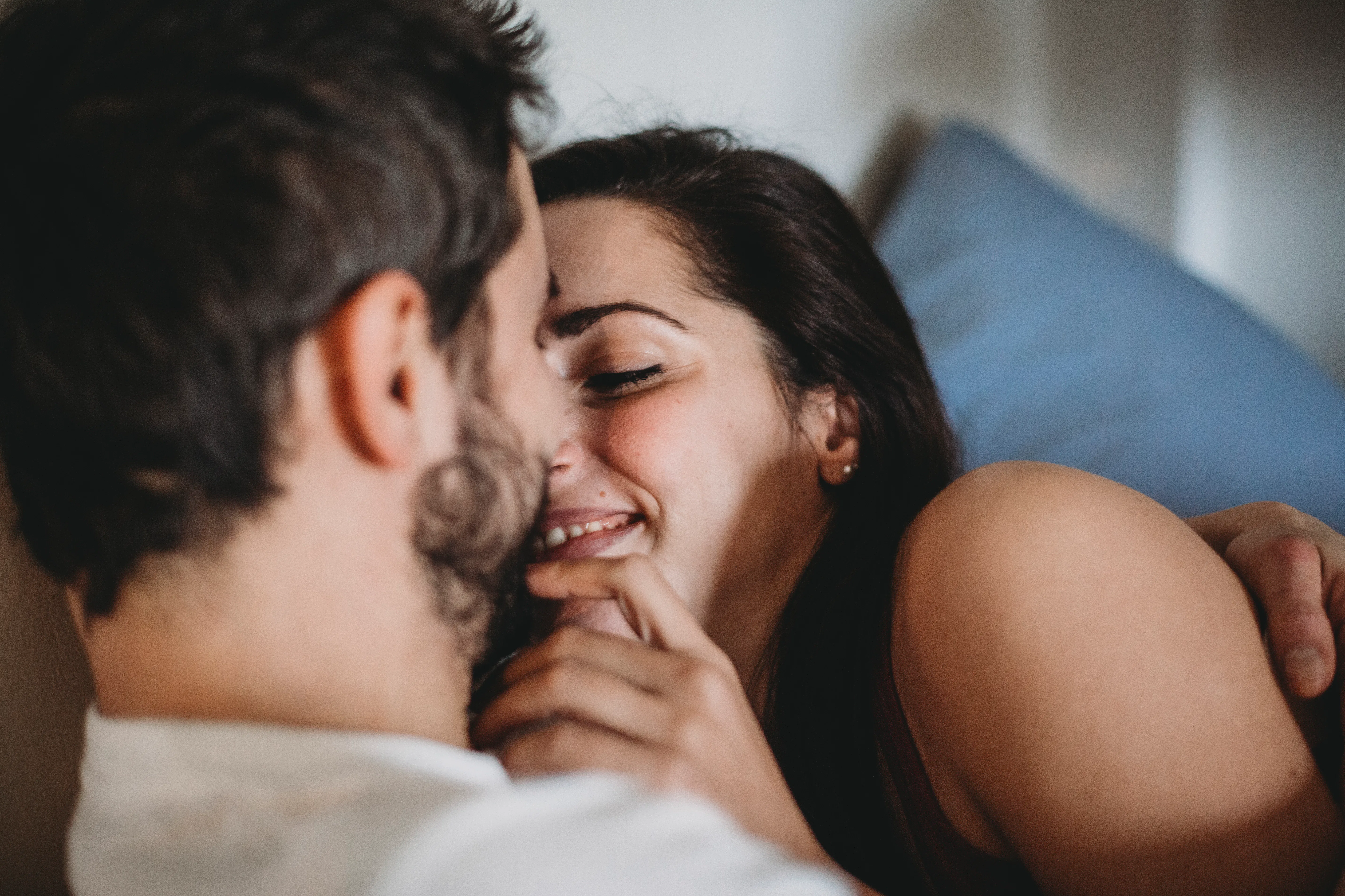Close-up of a smiling couple cuddling on a couch, woman leaning in toward a bearded man with hands g...