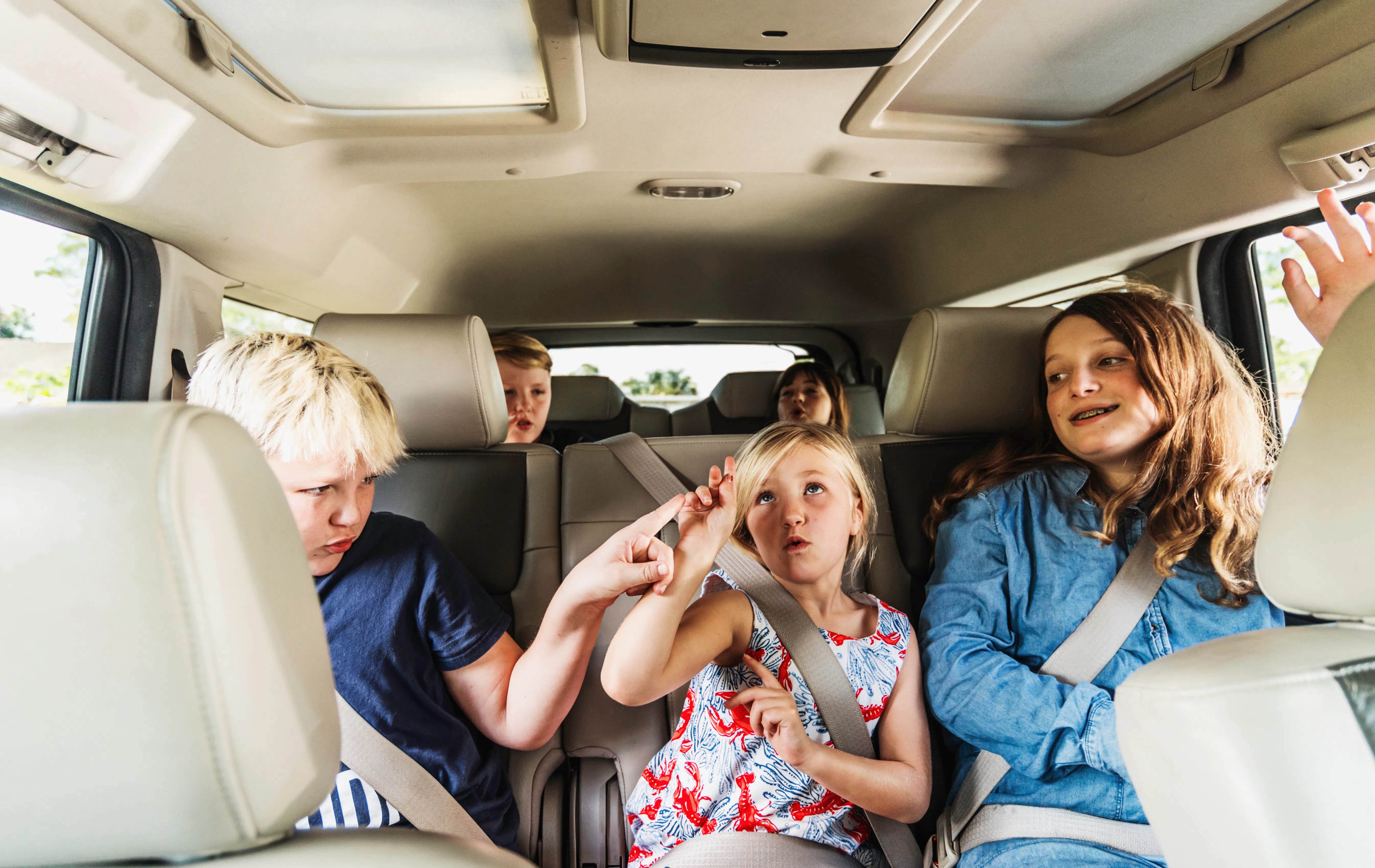 Silly fun happy group of kids in the backseat of a car singing and dancing with joy 
