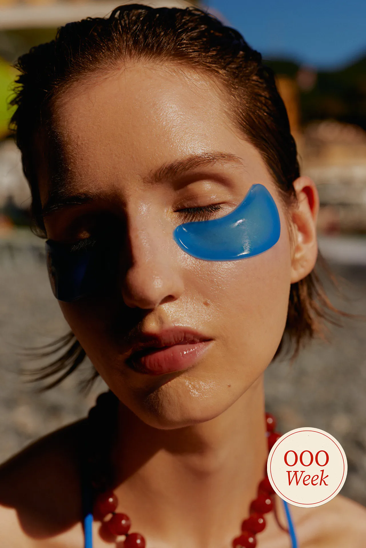 Woman on beach with blue under eye patches and red beaded necklace