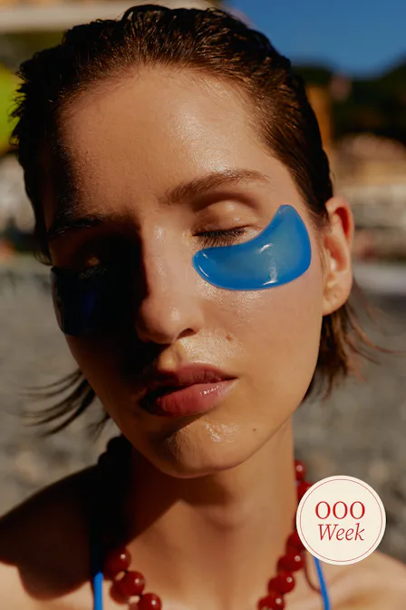 Woman on beach with blue under eye patches and red beaded necklace