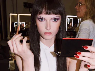alex consani in a brunette wig putting on makeup